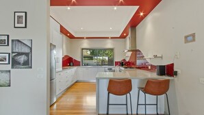 A modern kitchen with a central island, white cabinets, and a red accent wall.