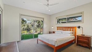A bedroom with a bed, bedside tables, a ceiling fan, and a large sliding glass door leading to a garden.