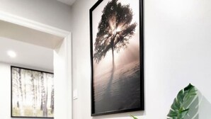 A hallway with a framed artwork of a tree, a potted plant, and a black sofa in the background. - The Cozy Cove Modern King-Bedroom Full Apartment (St. Catharines)