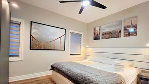 A hotel room with a bed, a ceiling fan, and three wall-mounted pictures. - The Cozy Cove Modern King-Bedroom Full Apartment (St. Catharines)