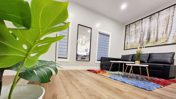 A modern living room with a wooden floor, a black sofa, a coffee table, a colorful rug, and a large painting on the wall. - The Zen Escape Modern Queen-Bed Full Apartment (St. Catharines)