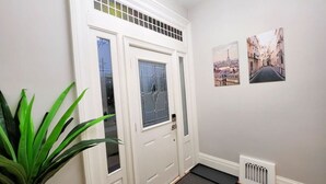 A hallway with a white door, a radiator, and two framed pictures on the wall. - The Zen Escape Modern Queen-Bed Full Apartment (St. Catharines)