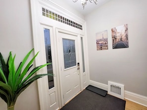 En hall med en vit dörr, ett element och två inramade tavlor på väggen.