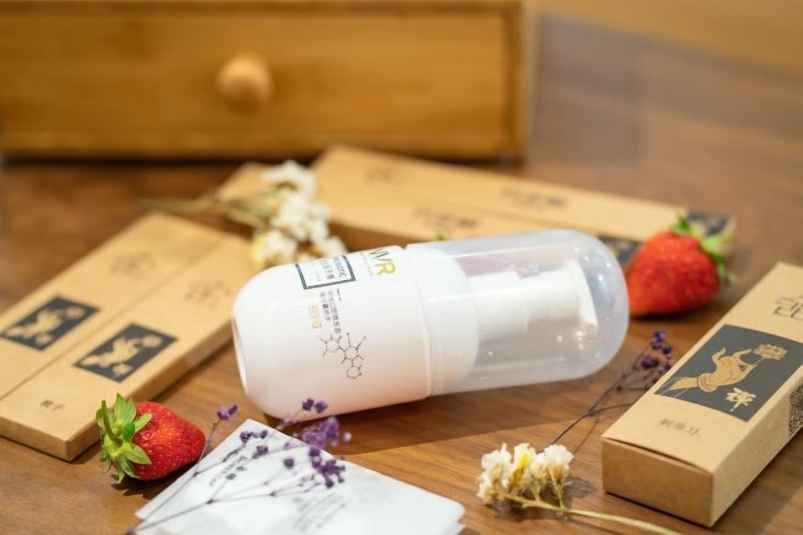 A wooden table with a white bottle, a strawberry, and some dried flowers.
