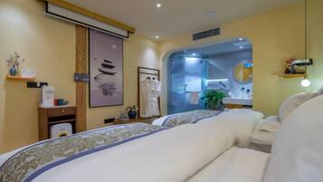 Quarto de hotel com cama, escrivaninha, espelho e chuveiro.