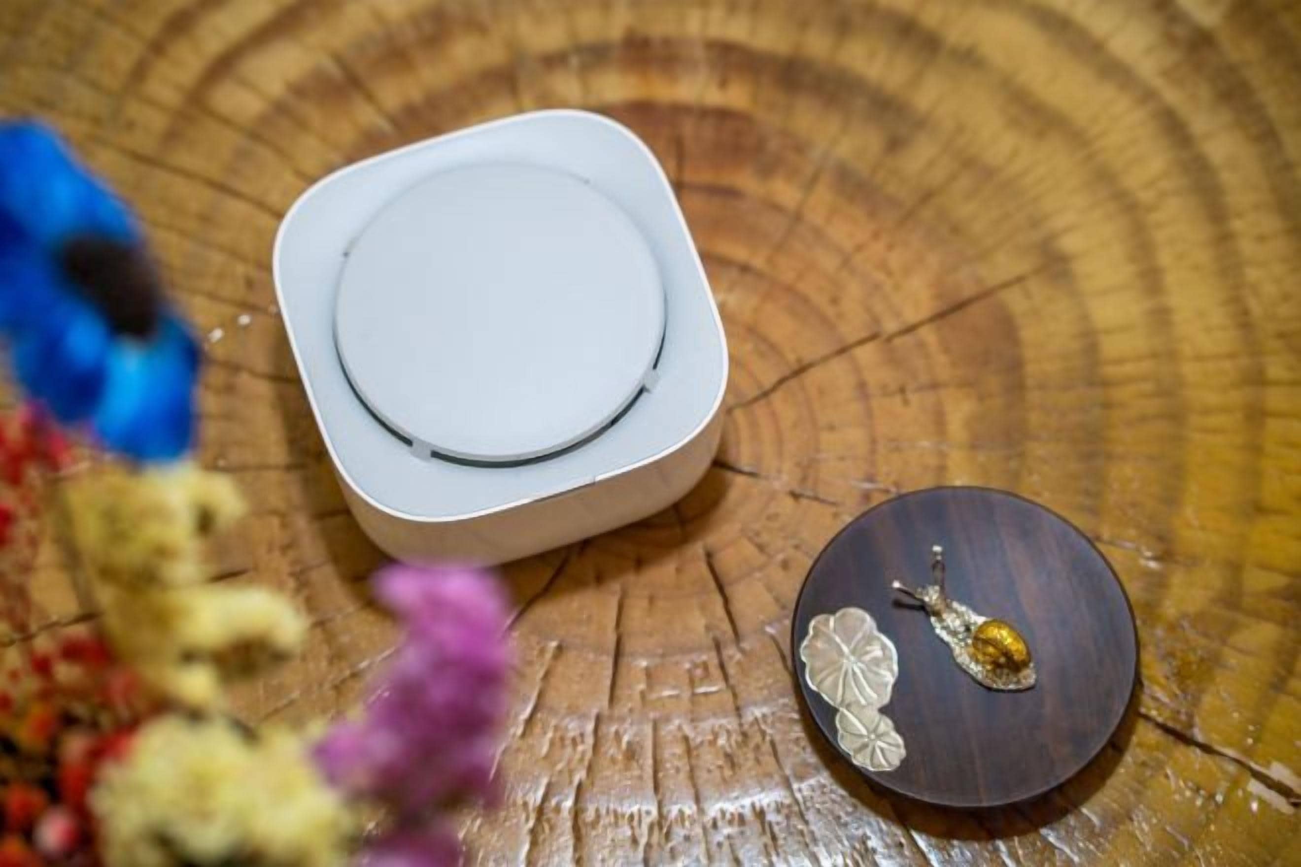 Une surface en bois sur laquelle se trouvent un objet carré blanc et un petit objet rond orné d’un élément décoratif.