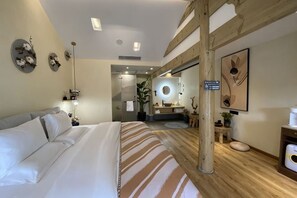 Ein Hotelzimmer mit einem großen Bett, Holzboden, einem Badezimmer mit Spiegel und einer kleinen Sitzecke.