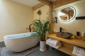 A modern bathroom with a freestanding bathtub, a round mirror with a light, a wooden vanity, and a potted plant. - Lijiang Shechen Inn (Lijiang)