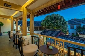 Un balcón de estilo tradicional con barandillas de madera, vista a edificios típicos y una mesa con un florero.