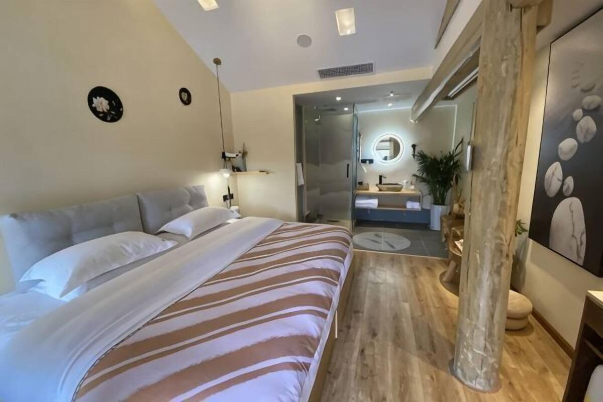 A modern bedroom with a large bed, a bedside table, a mirror, and a view into the bathroom.