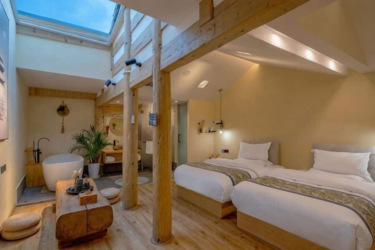 A bedroom with a skylight, wooden beams, a large bed, bedside tables, and a bathroom with a bathtub.