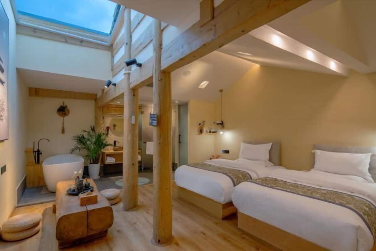 A room with a skylight, wooden beams, a bed, a large white chair, and a small table.