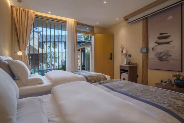 Habitación de hotel con dos camas, una ventana con cortinas, una mesita con lámpara y un cuadro en la pared.