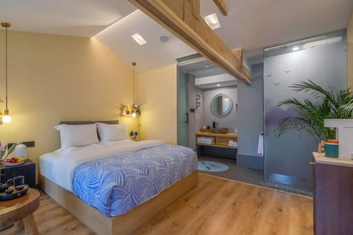 A modern hotel room with a large bed, a wooden ceiling, a round mirror, and a bathroom with a glass shower.