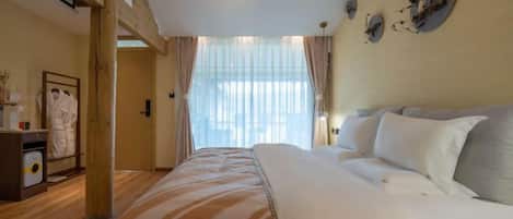 A hotel room with a bed, a wooden floor, a window with curtains, and a wall-mounted clock.