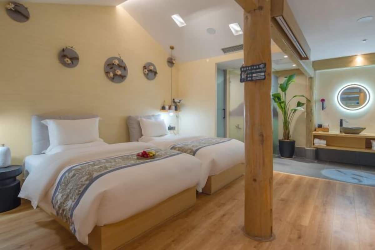 A hotel room with two beds, a wooden floor, a round mirror, a sink, and a potted plant.