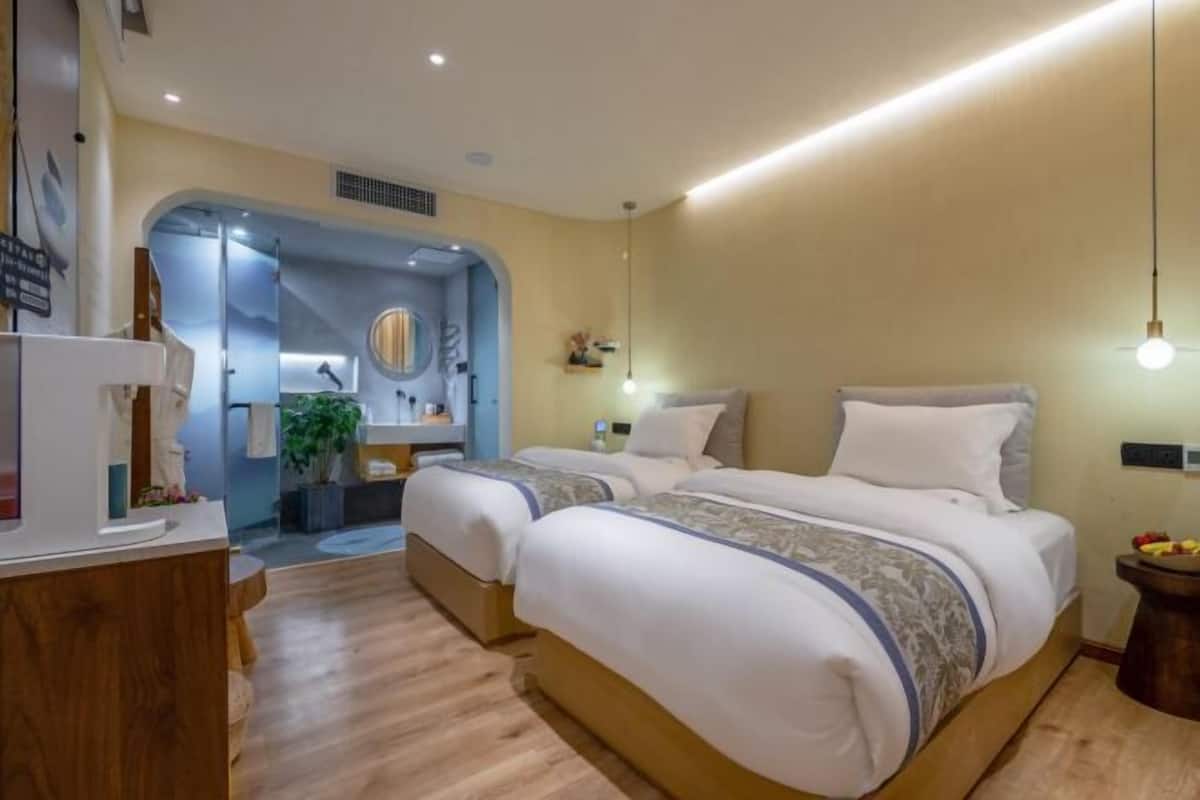 A hotel room with two beds, a wooden desk, a mirror, and a small plant.