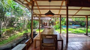 A wooden dining area with a view of a garden and a pool. - Villa Bhuvana with Private Swimming Pool (Gili Trawangan)