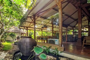 An outdoor covered area with a large decorative pot, a thatched roof structure, and a seating area with tables and chairs.