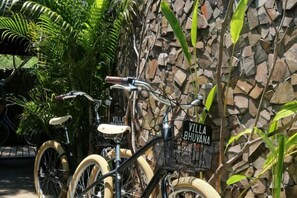 Una bicicleta con una cesta y un cartel que dice 'Villa Bhujana' apoyada contra una pared de piedra.