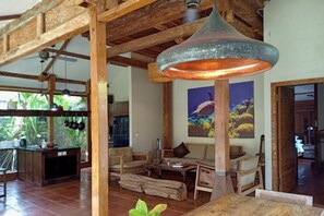 Un vaste espace de vie doté d’un plafond haut, de poutres en bois, d’un grand luminaire suspendu, d’un canapé, d’une table basse et d’un tableau accroché au mur.