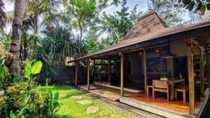 A modern house with a glass exterior, a wooden deck, and a garden with rocks and plants. - Villa Bhuvana with Private Swimming Pool (Gili Trawangan)