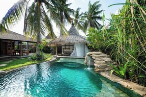 A pool with a waterfall, surrounded by lush greenery and a thatched-roof structure. - Villa with Private Swimming Pool Gili Trawangan (Gili Trawangan)