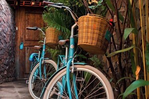 Deux vélos équipés de paniers en osier sont garés contre un mur, avec une porte en pierre en arrière-plan.