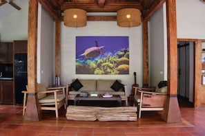 A room with a large wall mural, a sofa, two armchairs, a coffee table, and a wooden floor. - Villa with Private Swimming Pool Gili Trawangan (Gili Trawangan)