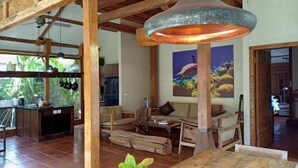 A spacious living area with a wooden ceiling, a large pendant light, a sofa, a coffee table, and a view of the outdoors. - Villa Bhuvana with Private Swimming Pool (Gili Trawangan)