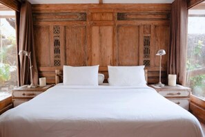 A double bed with white linens, wooden headboard with carved details, bedside lamps, and a view of greenery outside. - Villa with Private Swimming Pool Gili Trawangan (Gili Trawangan)