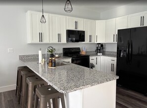Una cocina moderna con armarios blancos, encimeras de granito, un refrigerador negro y una estufa de acero inoxidable.