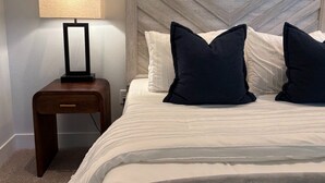 Een netjes opgemaakt bed met een houten hoofdbord, een nachtkastje met een lamp en twee kussens.