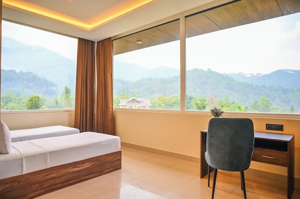 A room with a bed, a desk, and a view of mountains.