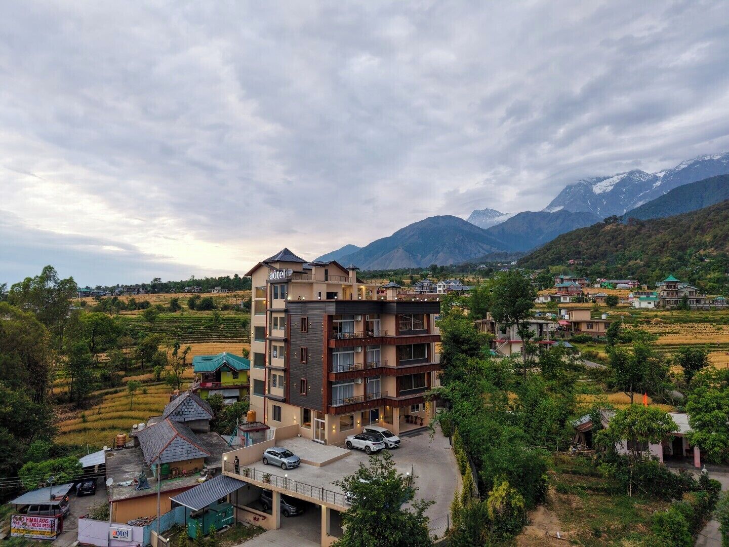 A multi-story hotel with a modern design, located in a hilly area with a view of mountains.