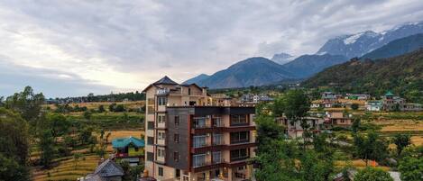 A multi-story hotel with a modern design, located in a hilly area with a view of mountains.