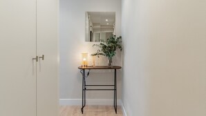 Un pasillo con una puerta blanca, una mesita con una lámpara y una planta en maceta.