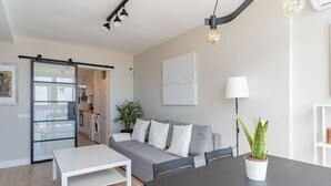 Una sala moderna con un sofá gris, una mesa de centro blanca y una mesa de comedor. Hay una planta en maceta sobre la mesa de comedor.