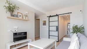 Una sala de estar moderna con un televisor de pantalla plana, muebles blancos, un ventanal corredero y una planta.