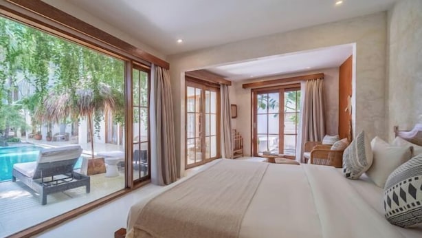 A bedroom with a large bed, a view of a pool, and a sliding glass door leading to a patio. - White Goose Boutique Hotel (Bali)