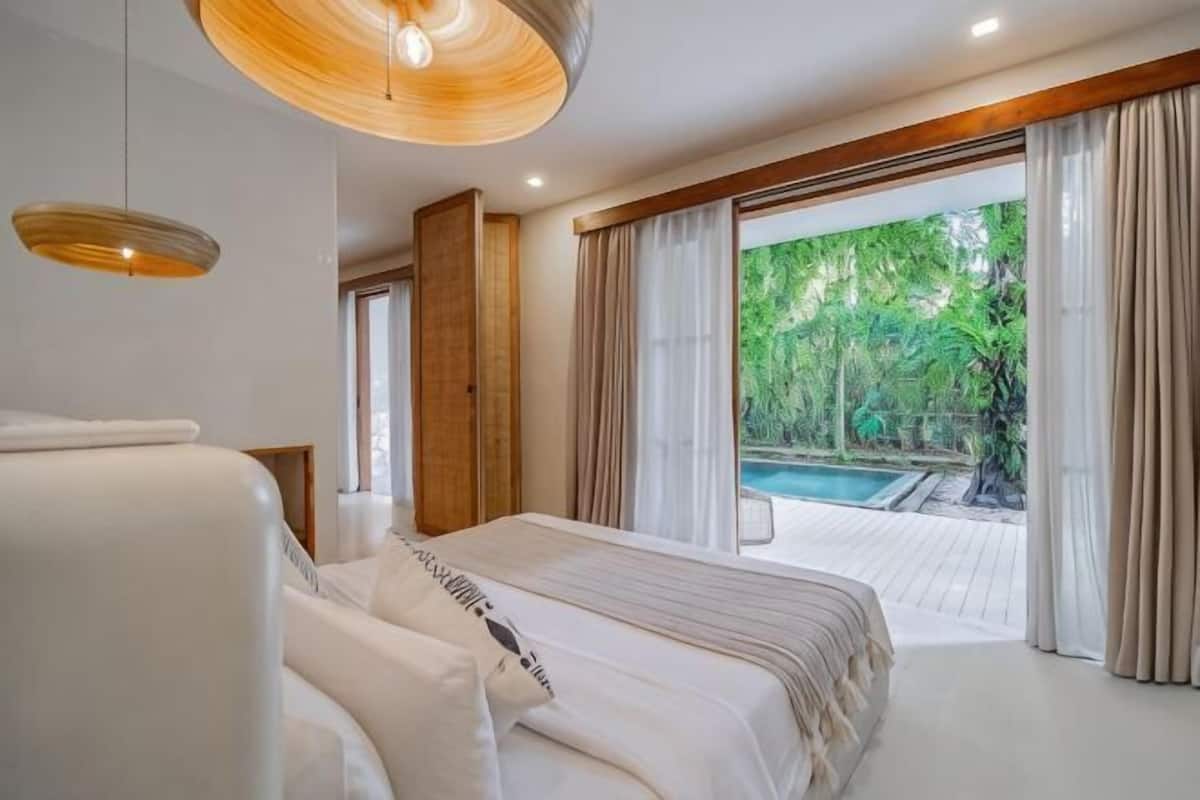 A bedroom with a large bed, a hanging light fixture, and a view of a swimming pool.