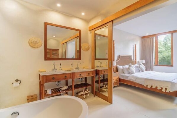 A modern bathroom with a freestanding bathtub, wooden vanity, and a large mirror. - White Goose Boutique Hotel (Bali)