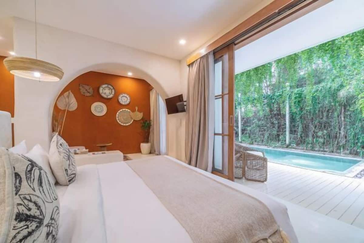 A bedroom with a large bed, a TV, and a view of a swimming pool.