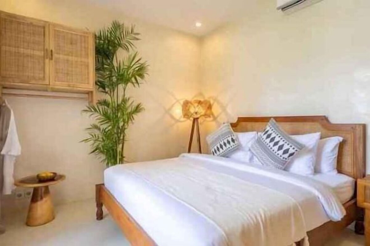 A neatly arranged bedroom with a bed, bedside table, lamp, and a potted plant.