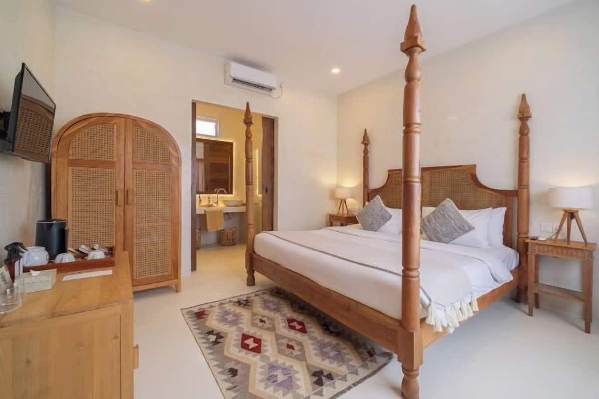 A bedroom with a four-poster bed, wooden wardrobe, and a mirror.