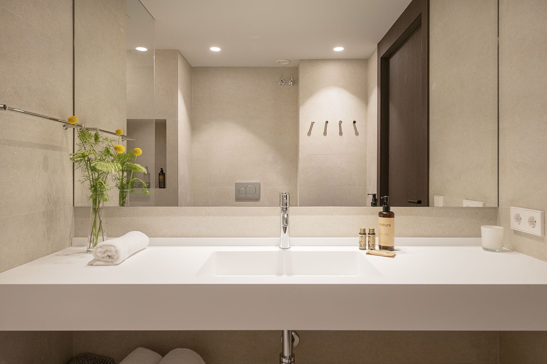 A modern bathroom with a large mirror, a white sink, and a towel rack.