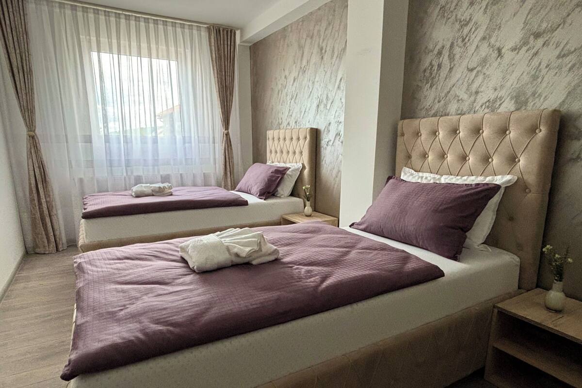 A hotel room with two beds, each with a tufted headboard and purple bedding.