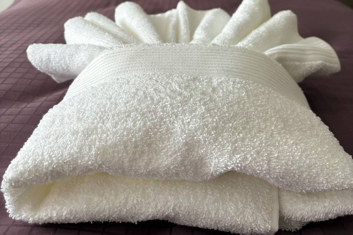 A bed with a tufted headboard, a purple pillow, and a white textured blanket.