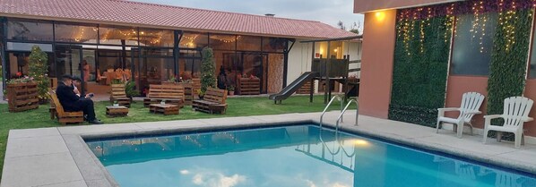 Un espace piscine avec des bancs et des chaises en bois, un toboggan et un sapin de Noël.