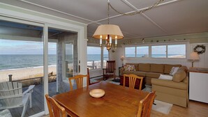 Un amplio salón con una mesa de comedor de madera, un sofá beige y vistas a la playa.